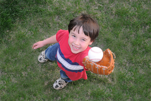 little boy in a red striped shirt catching a baseball in his mitt from the air